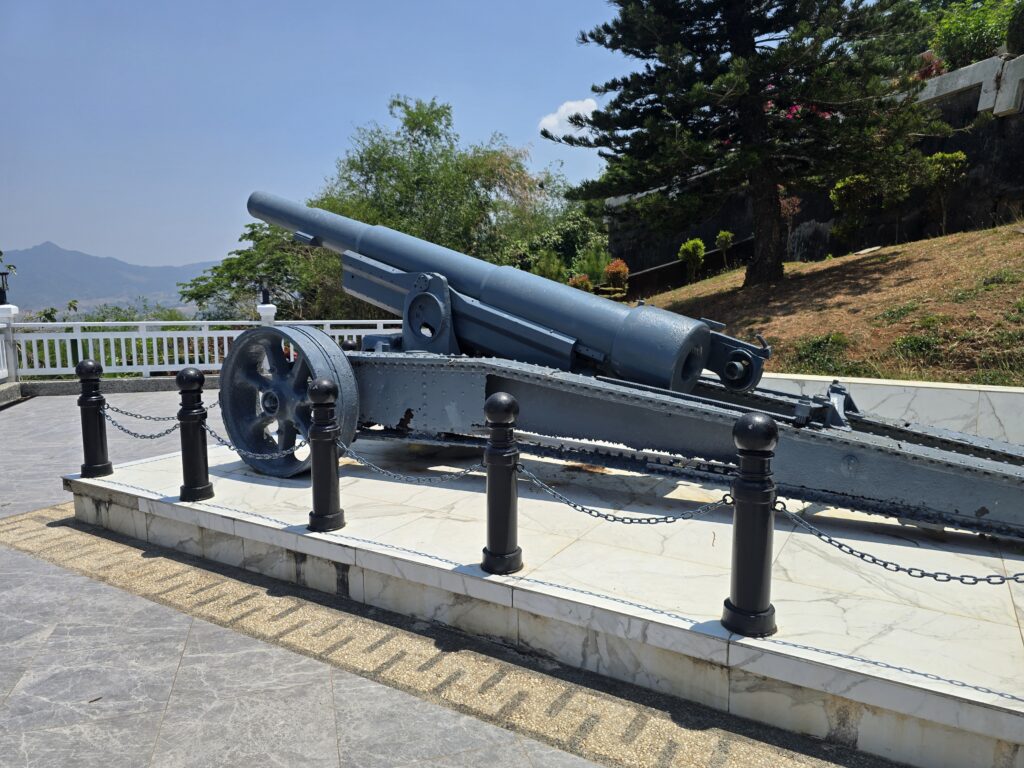 Historic cannon displayed on a marble platform with chains and bollards.
