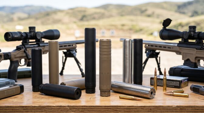 Rifles with scopes, silencers, and ammunition on a table at a shooting range.