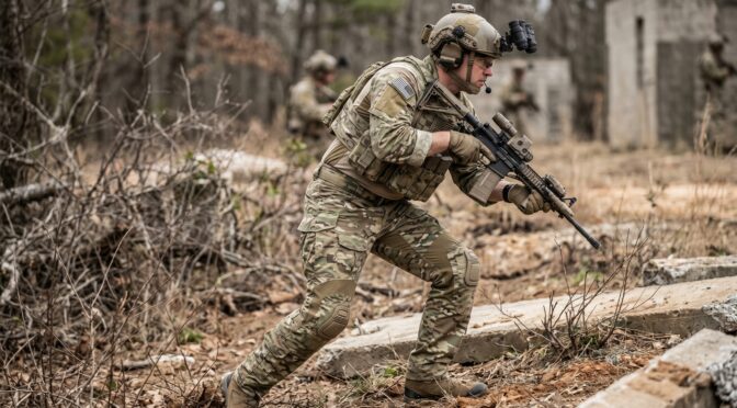 Soldier in camouflage gear with rifle moves through wooded terrain.
