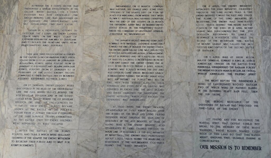 Text on a marble wall detailing WWII battles and troop movements in the Philippines.