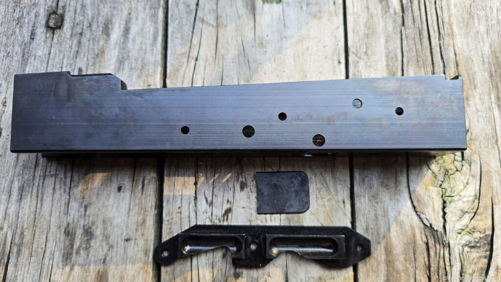 Black firearm receiver and parts on weathered wood surface