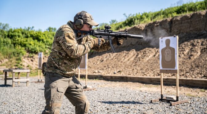 Man in camouflage fires a rifle at a target range, smoke from the muzzle.