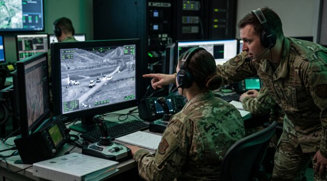 Airmen operate drone surveillance system, monitoring ground activity on screen.