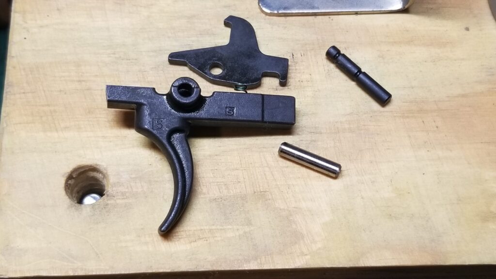 AR-15 trigger group parts: trigger, hammer, and pins on a wooden surface.