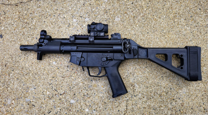 Black MP5-style firearm with red dot sight and adjustable stock